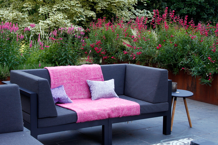 Modern comfortable garden furniture creates an outdoor social space surrounded by lush planting in corten steel planters
